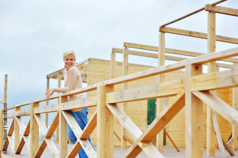 Outdoors portrait of beautiful emotional young blonde woman standing on the unfinished wooden deck and looking to side, smiling happily.