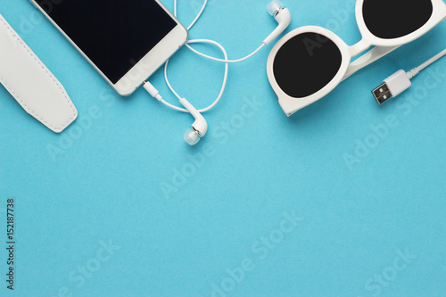 studio shot of white sunglasses smart phone and earbuds on blue background