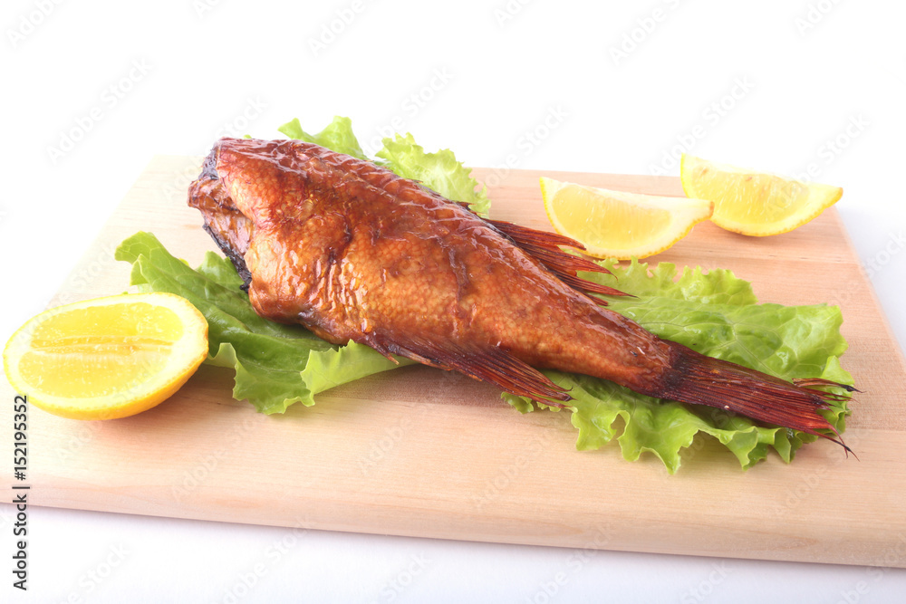 Smoked fish and lemon on green lettuce leaves on Wooden cutting board isolated on white background.