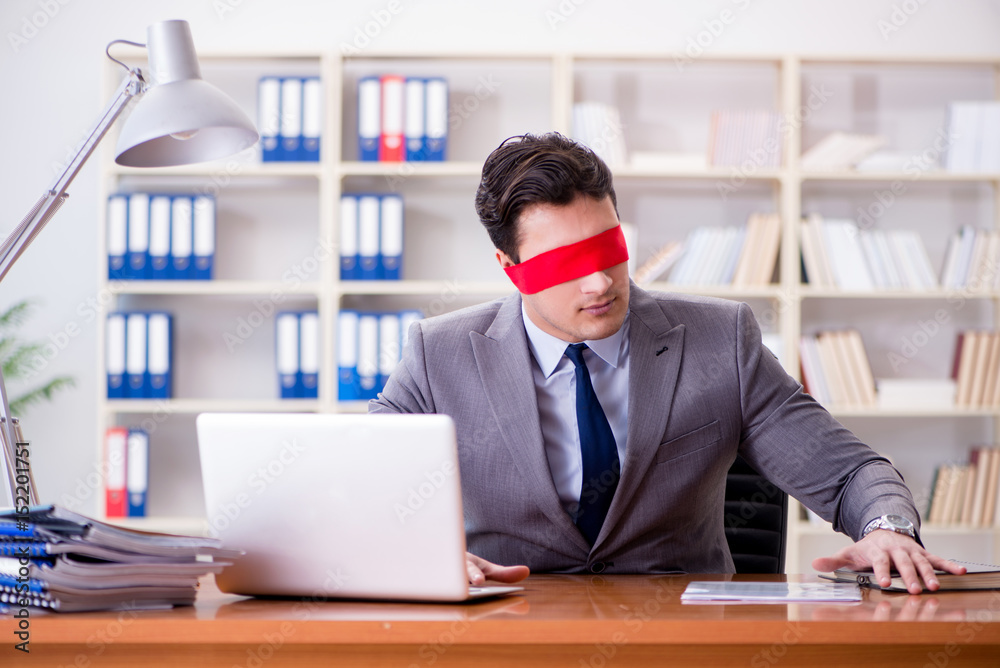 Blindfold businessman sitting at desk in office Blindfold businessman sitting at desk in office