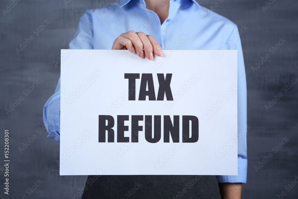 Woman holding paper sheet with text TAX REFUND on color background Woman holding paper sheet with text TAX REFUND on color background