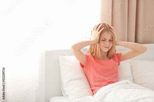 Cute girl suffering from headache while sitting on bed at home