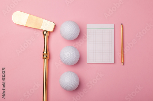 Fototapeta pusty notatnik, ołówek, luksusowy złoty klub golfowy z piłkami golfowymi na białym tle na różowym tle