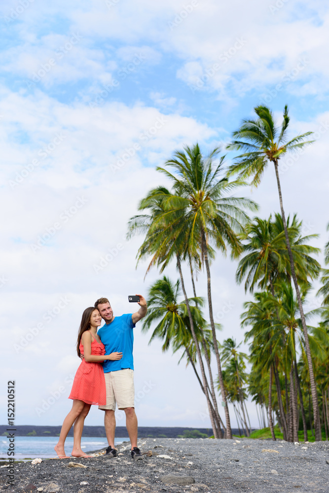 Selfie couple on nature travel Hawaii vacation black sand beach in Big island of Hawaii, USA. Hawaiian holidays getaway. Secluded beach off the beaten path.