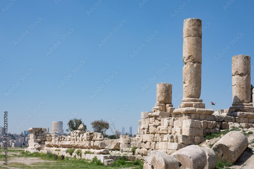 Ancient Roman ruins of the Temple of Hercules at Amman Citadel with a view of Amman city and the Jordanian flag in the background. Fallen blocks are in the foreground.