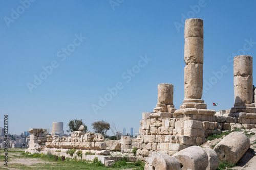 Ancient Roman ruins of the Temple of Hercules at Amman Citadel with a view of Amman city and the Jordanian flag in the background. Fallen blocks are in the foreground.