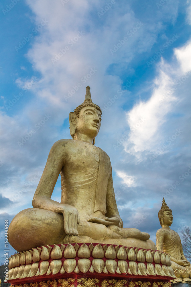 Large golden buddha statue shot from a low perspective with blue sky and clouds behind it Large golden buddha statue shot from a low perspective with blue sky and clouds behind it