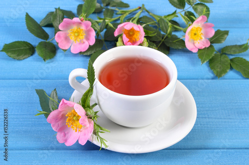 Cup of tea and wild rose flower on boards