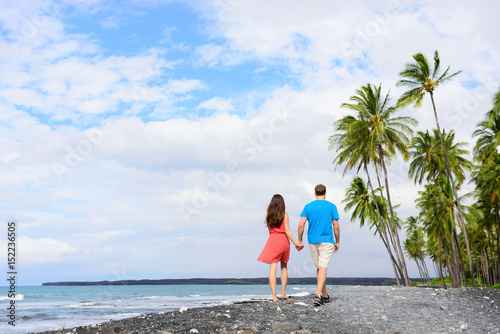 Vacation couple walking holding hands on beach travel destination. Happy summer holidays.black sand beach in Big island of Hawaii  USA.