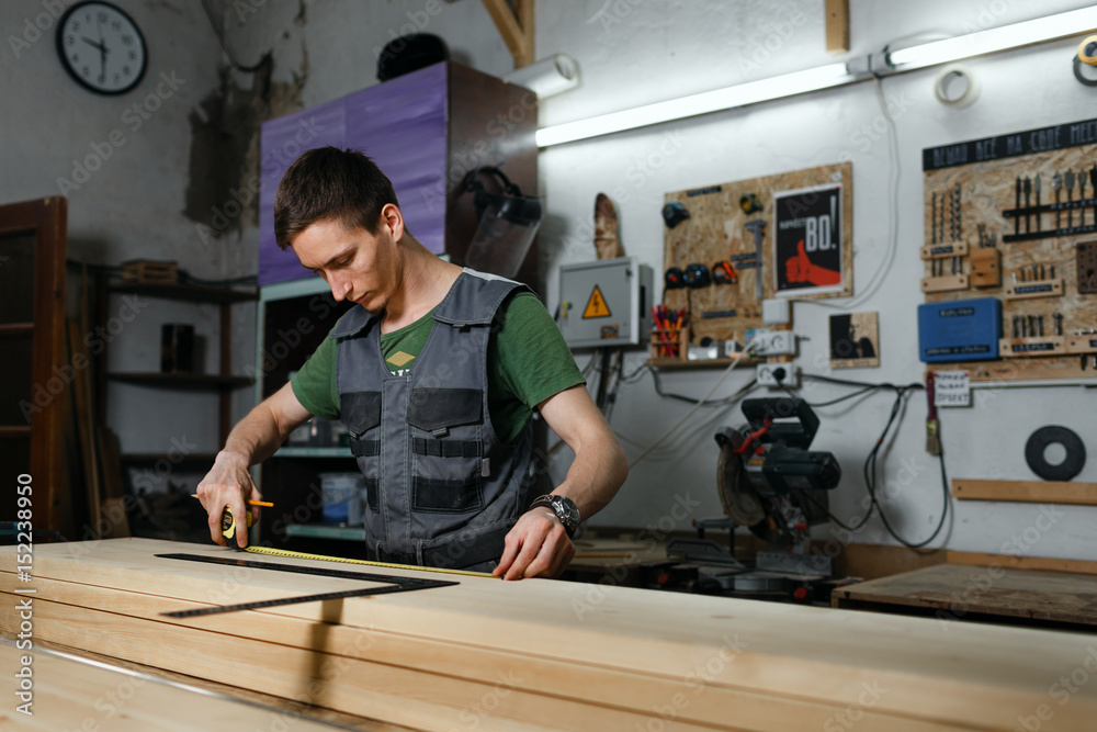 A professional carpenter in the workshop makes measurements of the product with a measuring tape measure