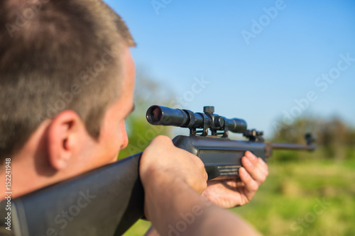 The man takes aim at the target with a sniper strikeball rifle. Selective Focus. Blue sky.