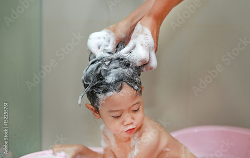 Mother's hand pours water from shower to wash little girl's hair.