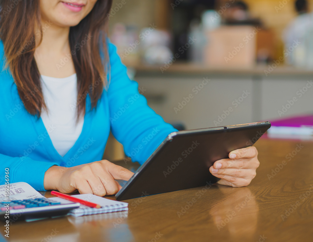 Pretty Young womans hands holding and using tablet for online shopping, bill, pencil and calculator on the table. Online payment. Female working on tablet in a cafe. Pretty Young womans hands holding and using tablet for online shopping, bill, pencil and calculator on the table. Online payment. Female working on tablet in a cafe.