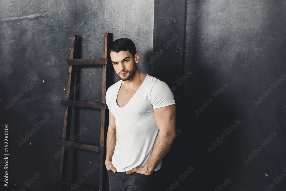 Portrait of young attractive man with muscular strong black beard, piercing sexy look in the studio posing t-shirt Portrait of young attractive man with muscular strong black beard, piercing sexy look in the studio posing t-shirt