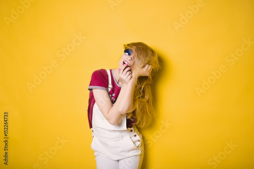 close-up portrait of a beautiful young hipster lifestyle slim blond girl in fashionable sunglasses on a yellow background in the studio in a white suit and shirt smiling and posing
