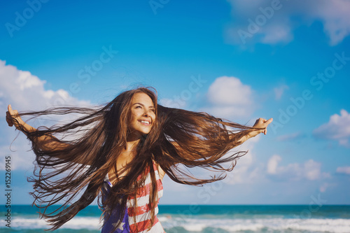 close-up portrait of a beautiful young brunette girl with long hair on a background of blue sea with waves and sky with clouds on a sunny day, lifestyle, posing and smiling, wind