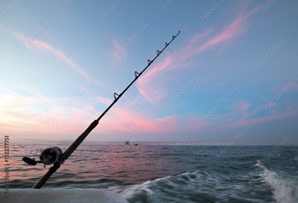Fishing rod on charter fishing boat against pink sunrise sky on