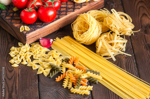 Assortment of raw types and shapes of italian pasta and wooden board on a black slate background. Close up. Top view and copy space.