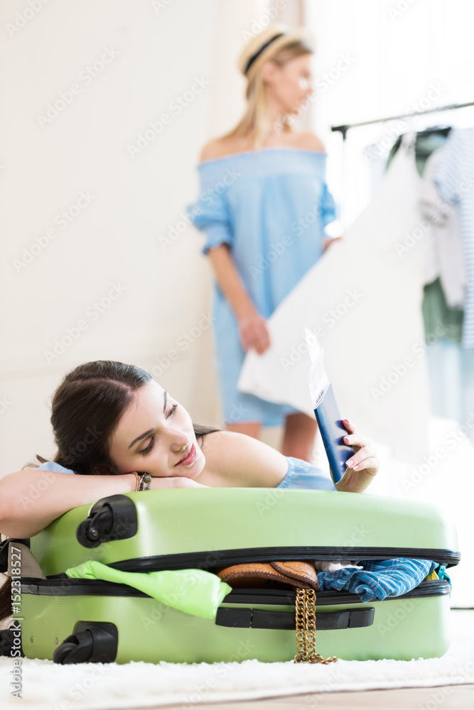 Smiling young woman leaning on suitcase and holding passports and tickets, packing luggage concept Smiling young woman leaning on suitcase and holding passports and tickets, packing luggage concept