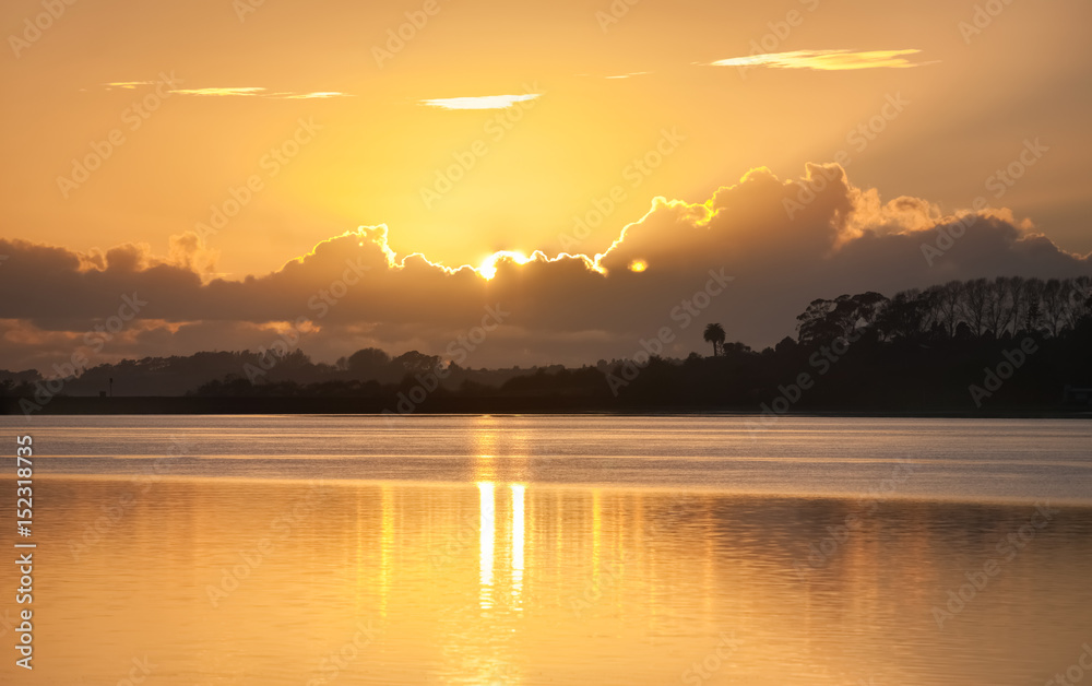 Glow of rising sun behind clouds across bay.