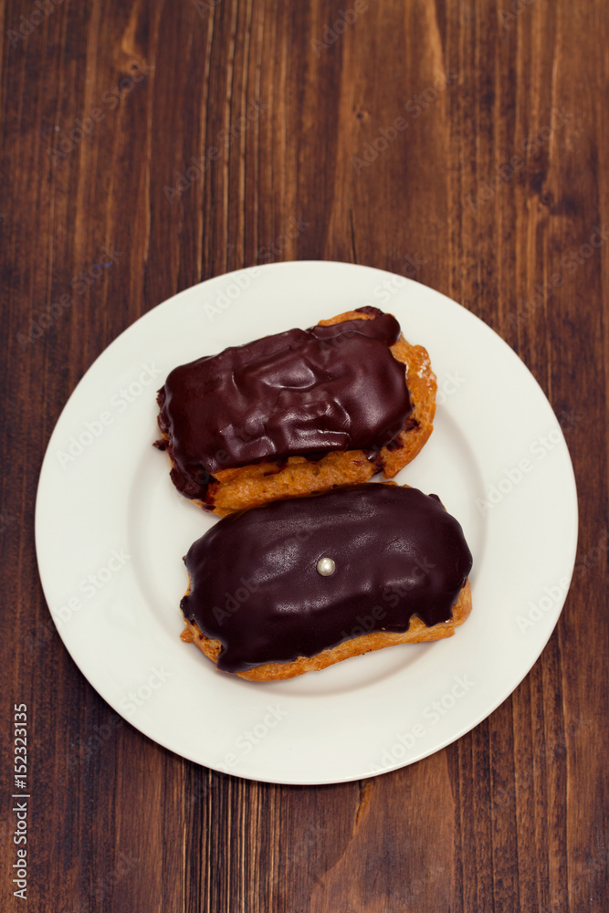 chocolated eclairs on white dish on wooden background chocolated eclairs on white dish on wooden background