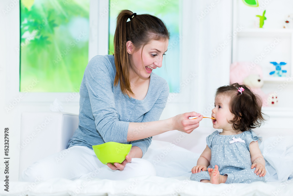 Mother feeding her baby little girl with a baby food .Baby smiling and like that sweet taste.Shallow doff