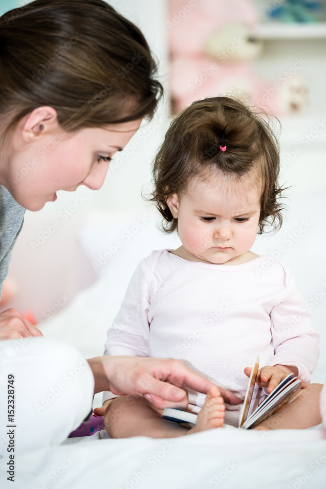 Baby little girl looking at book while mom reading the interesting story and showing the pictures .Shallow doff Baby little girl looking at book while mom reading the interesting story and showing the pictures .Shallow doff