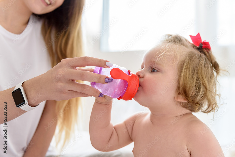 Thirsty baby girl drinking water from mother hands