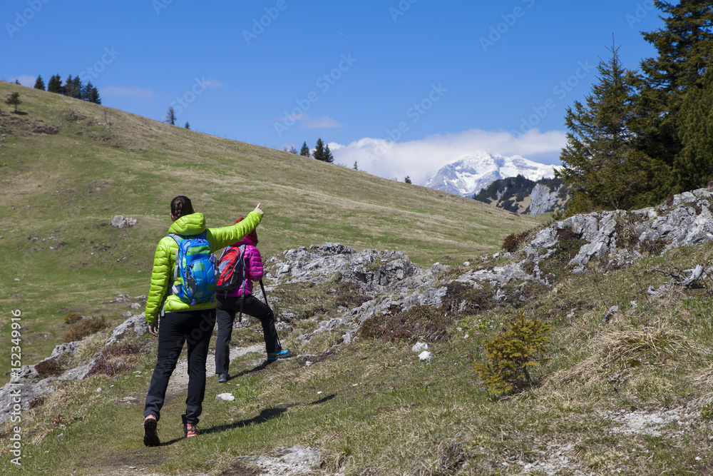 Hikers walking on hike in mountain nature landscape in Slovenian Alps and pointing on mountain peak. Hiking – sporty hiker women on trek with backpack living healthy active lifestyle. 