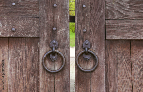 Ancient closed wooden gate with two door knocker rings