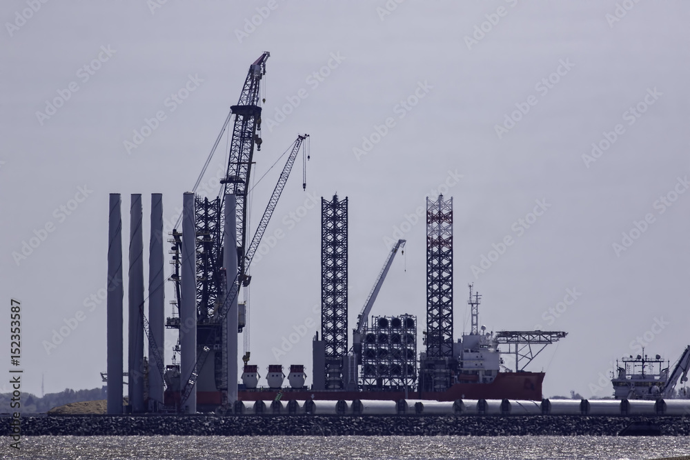Offshore wind farm turbine construction. Supply vessel ship docked at an outer harbour to be loaded with wind turbine parts. Clean energy investment.
