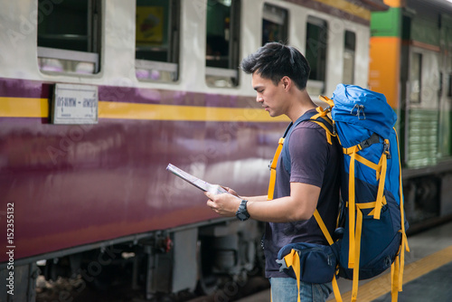 Traveler wearing backpack holding map on railway at train station photo