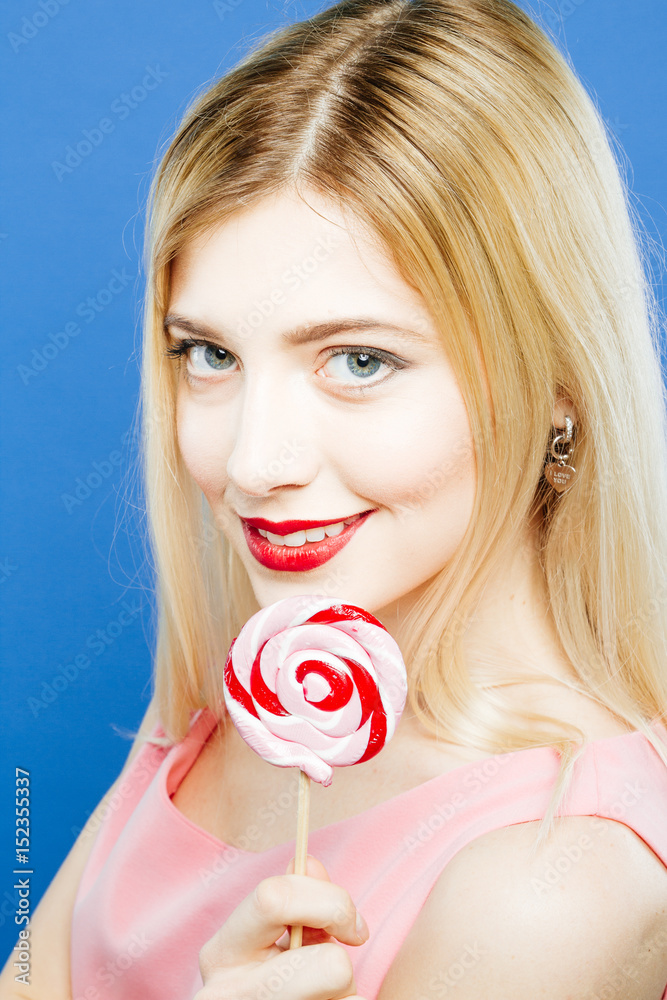 Closeup Portrait of Cute Blond-haired Girl with Colorful Lollipop in Hands on Blue Background in Studio.