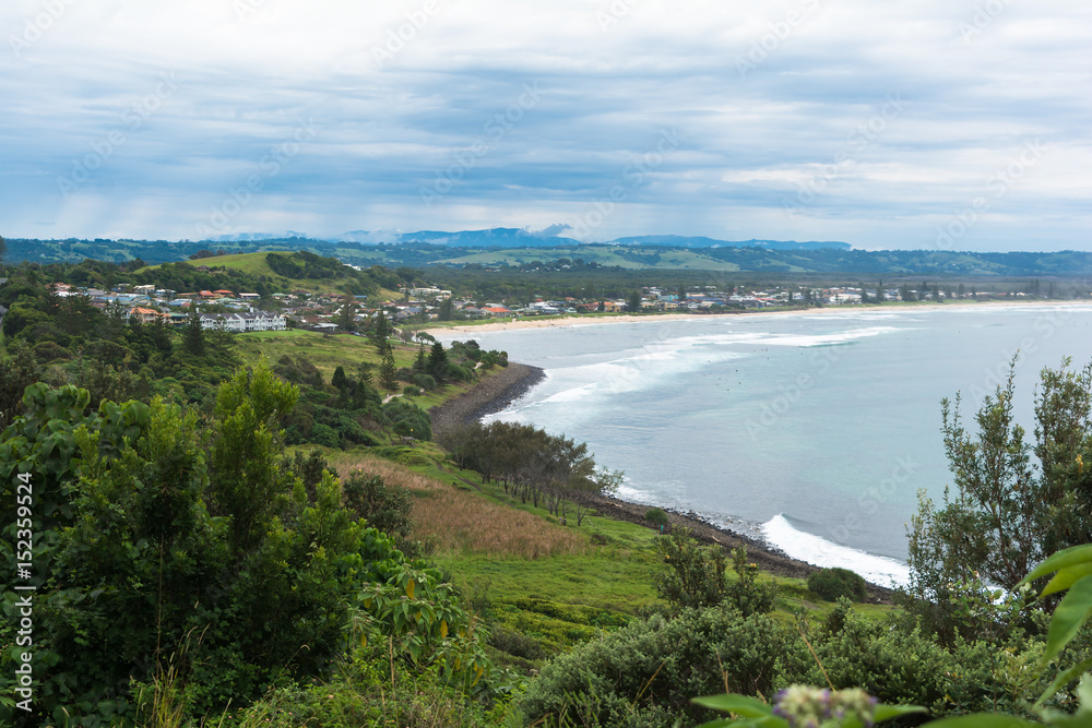 The view from the hill with bush on the ocean with surfers and mountains and horizon with cumulus clouds and stormy grey sky in Ballina, Byron Bay, Australia