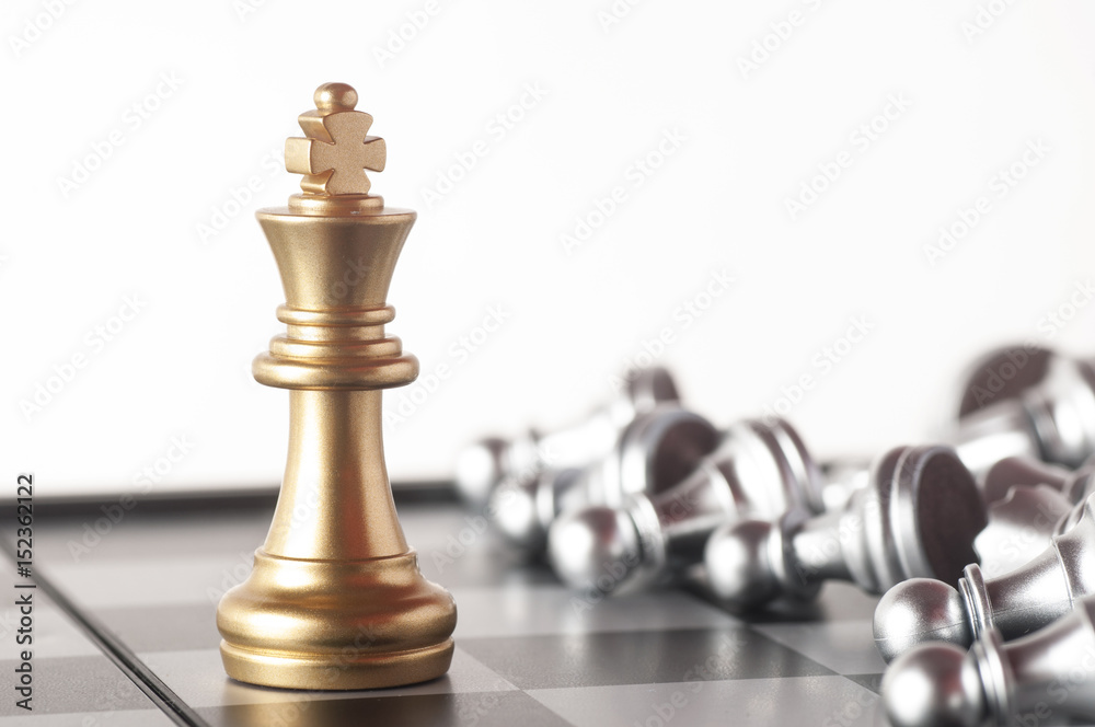 Gold king on a chess board surrounded by a number of fallen silver chess pieces with selective focus Gold king on a chess board surrounded by a number of fallen silver chess pieces with selective focus