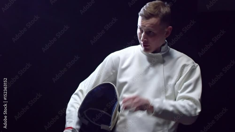 Professional fencer holding foil and mask while taking a break during fight with opponent Professional fencer holding foil and mask while taking a break during fight with opponent