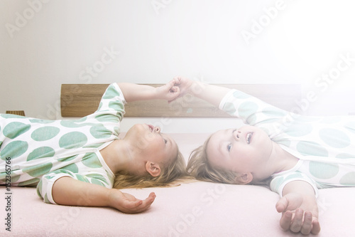 Fotografia Two charming and strongly similar twins girls lie on a big bed and dream of adve