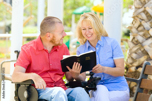 Disabled man with his wife fiilng happy while reading holy bible at the park