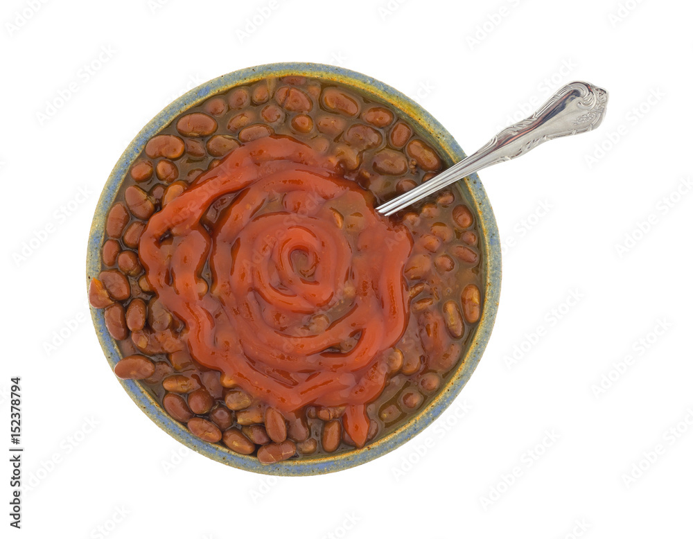 Bacon onion flavored baked beans with ketchup in a bowl with a spoon in the food isolated on a white background.