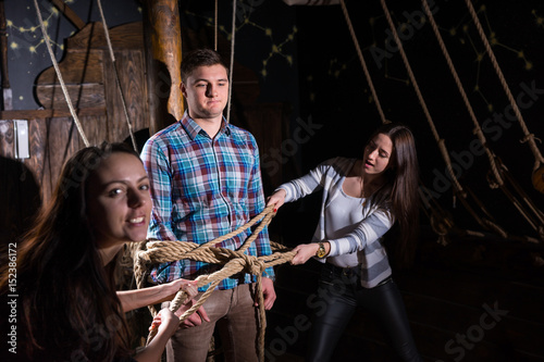 Attractive girls tie a young guy to a column on the deck of a ship photo