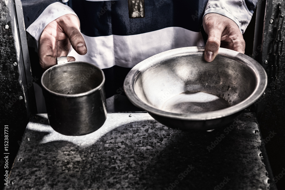 Male prisoner's hands holding aluminum dishes in a hole for supplying food