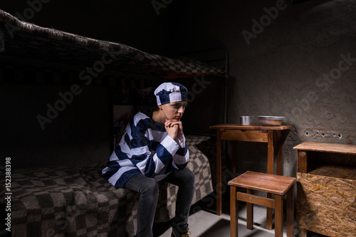 Bilde på lerret Young female prisoner wearing prison uniform has lost in thought while sitting o