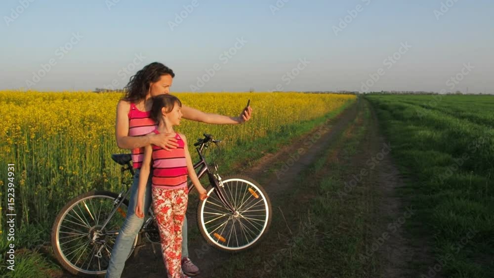 Woman with a child doing selfie in nature. A happy mother with her daughter is photographed in the countryside. Cyclists make selfies. Sports family on a field of yellow flowers. Rapeseed field. Woman with a child doing selfie in nature. A happy mother with her daughter is photographed in the countryside. Cyclists make selfies. Sports family on a field of yellow flowers. Rapeseed field.