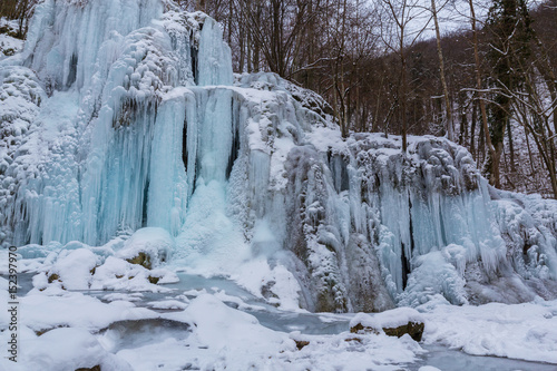 Wild river, beautiful frozen waterfalls and fresh snow in a mountain forest, on a cold winter day