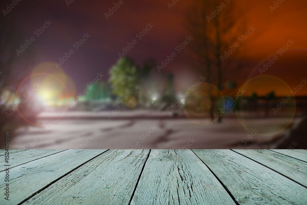 Image of wooden pattern table in the front, abstract winter background blurred landscape in evening light of a lantern Image of wooden pattern table in the front, abstract winter background blurred landscape in evening light of a lantern
