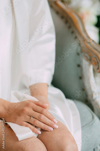 bride in a robe sits on the bed with her hands clasped  on the finger of the bride the wedding ring
