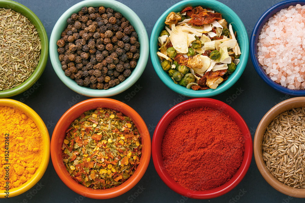Spices in colorful bowls viewed from above. Various seasonings on a dark background. Italian mix, cumin, chili pepper, curry powder, Himalayan salt, pepper, garlic, cinnamon, dried tomato. Top view