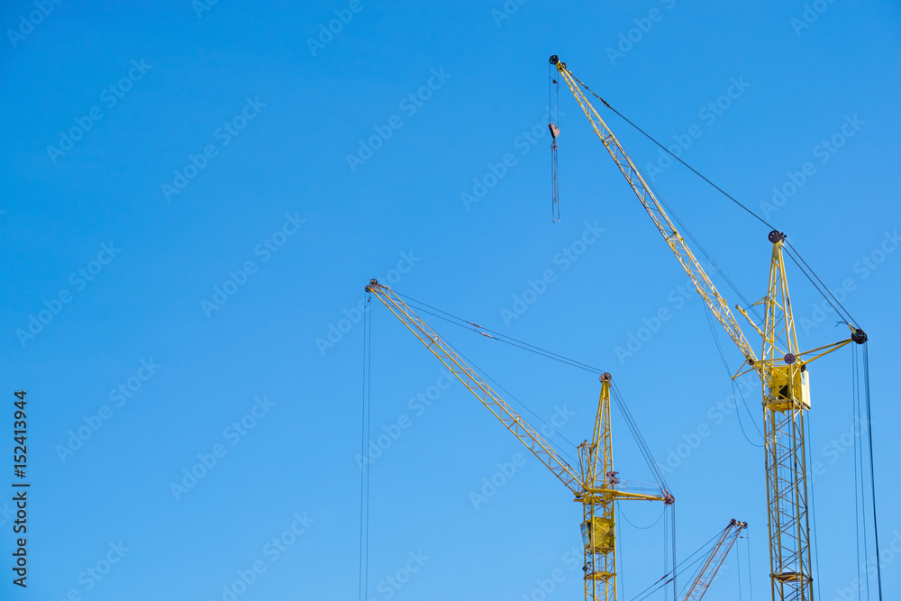 The yellow cranes at the construction site against the blue sky