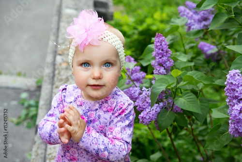 Beautiful little girl happy smiling and claps her hands over lilac flowers in spring park. Childhood. Cute kid's face over nature background. Cheerful child's portrait, soft focus.