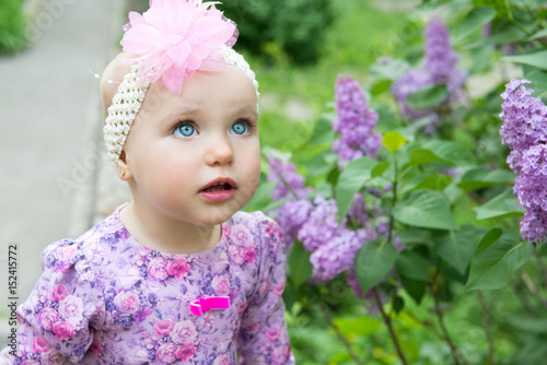 Beautiful little girl smells lilac flowers in spring park. Childhood. Cute kid's face over nature background. Cheerful child's portrait, soft focus.